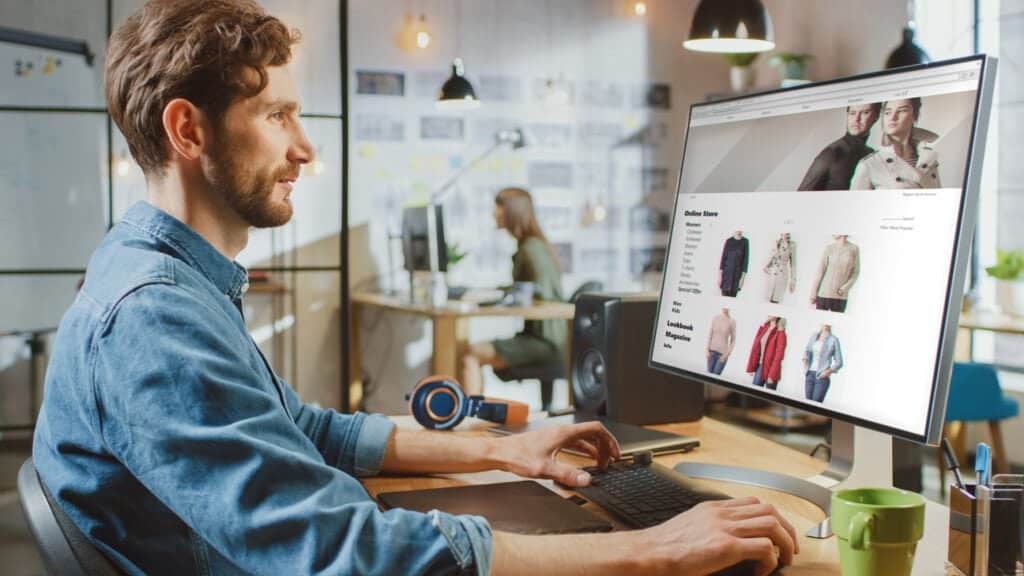 High-quality web design work displayed on a desktop monitor featuring an online store with clothing products in a modern, creative office environment.