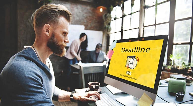 Deadline reminder on computer screen at stylish modern workspace with team members in background.