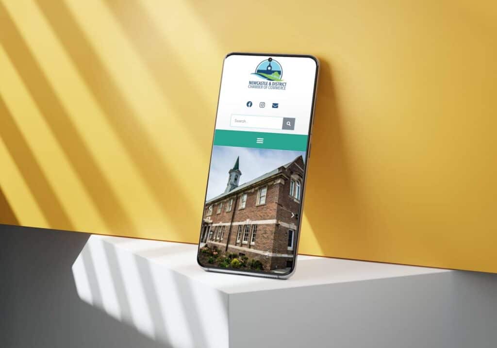 Modern smartphone displaying a website for the Newcastle & District Chamber of Commerce against a yellow background.