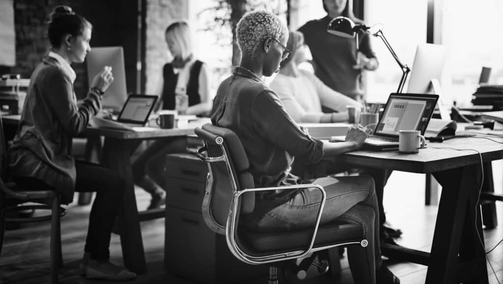 Modern diverse team working on web design project in an office, using laptops and digital tablets, collaborating creatively in a professional environment.