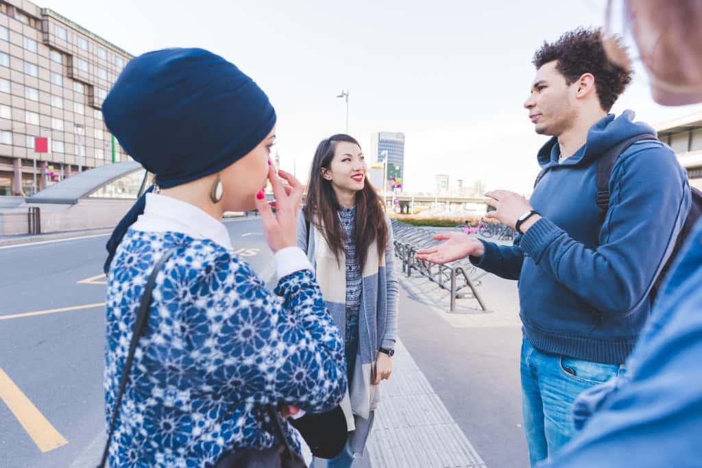 Someone explaining directions to a diverse group of friends on a city street in Oshawa, Ontario, with modern buildings and urban infrastructure in the background, emphasizing local community and communication.