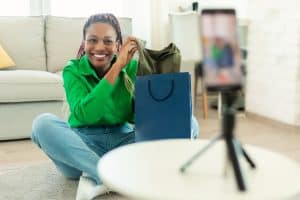 Bright smiling woman recording product review for web design services in Durham Region, sitting on living room floor with shopping bags.