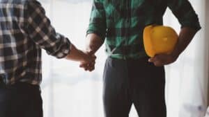Two construction professionals shaking hands, one holding a yellow safety helmet, symbolizing partnership and trust in Durham Region's contractor and trades websites.