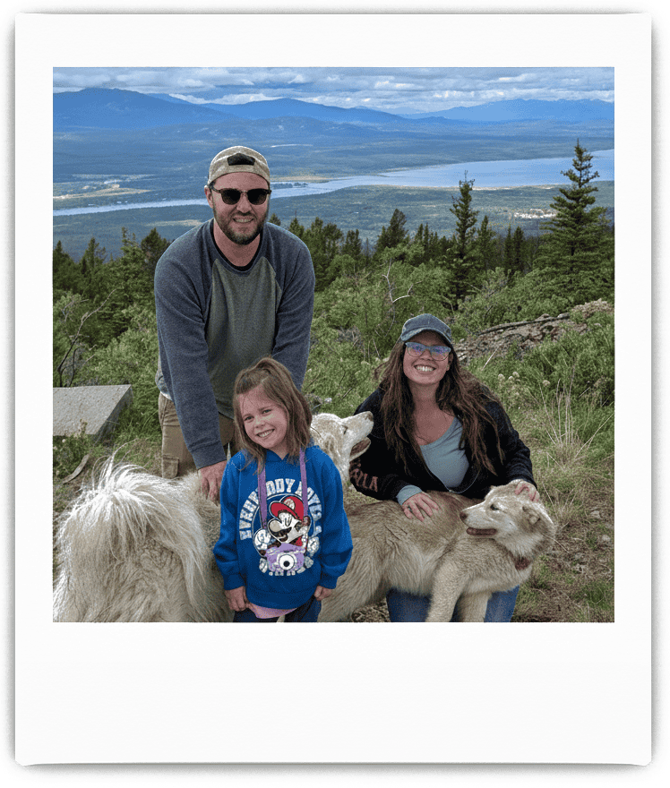 A family enjoying their time outdoors with dogs in a lush mountain landscape, featuring a background of trees, a lake, and distant mountains under a partly cloudy sky. Perfect for showcasing outdoor activities and adventure near Oshawa and Durham Region.