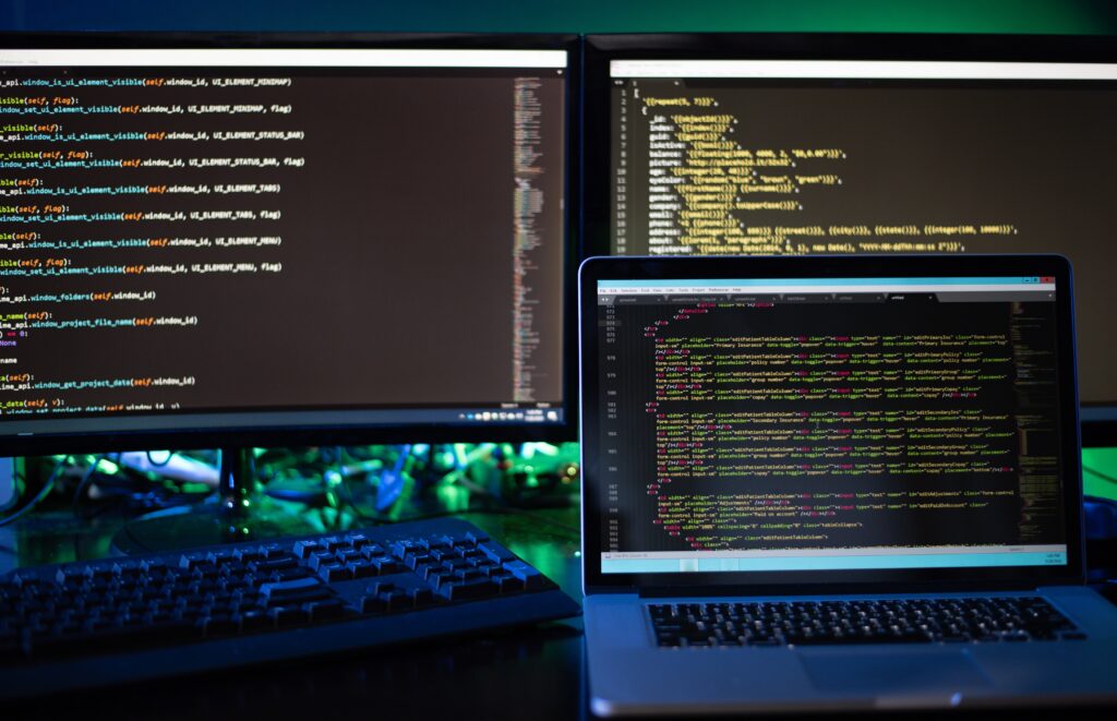 Two computer screens and a laptop displaying code and programming scripts for web development and security.